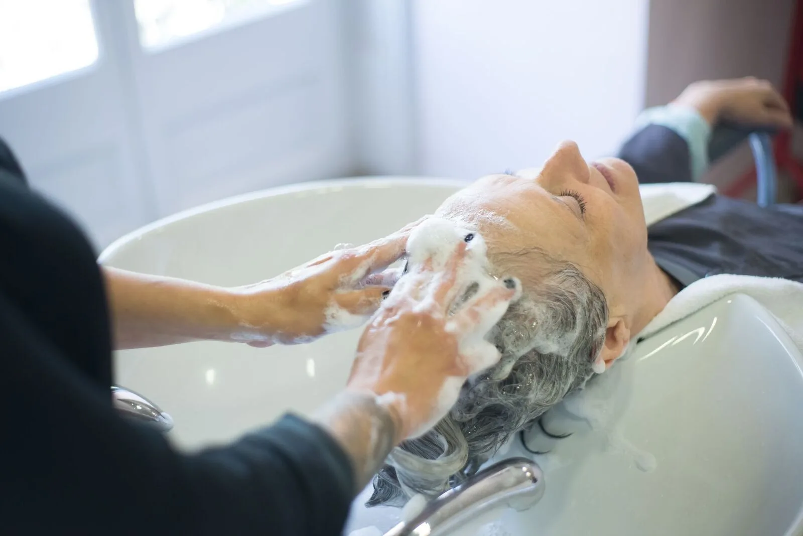 Warm water and lather worked through a client's hair over the head spa basin