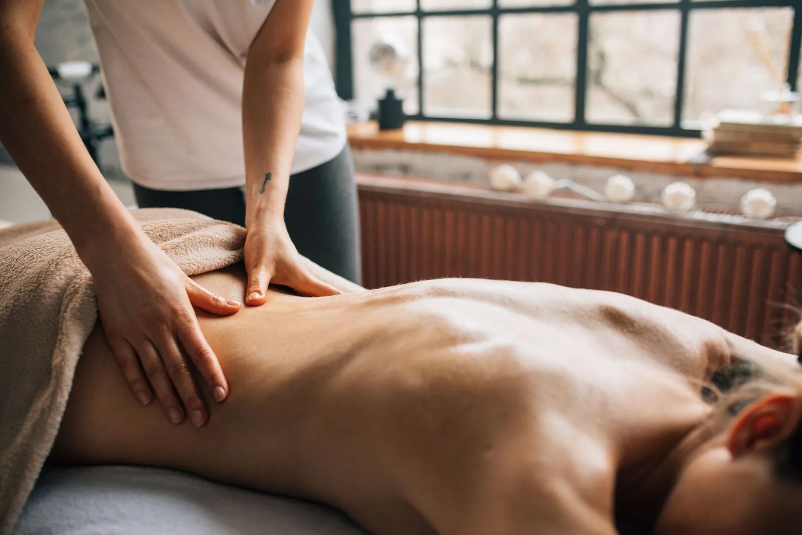 A therapist giving a slow full-body massage beside a bright window